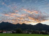 Blick über das abendliche Aschau mit leuchtenden, verzerrten Wolkenhaufen über den Bergen